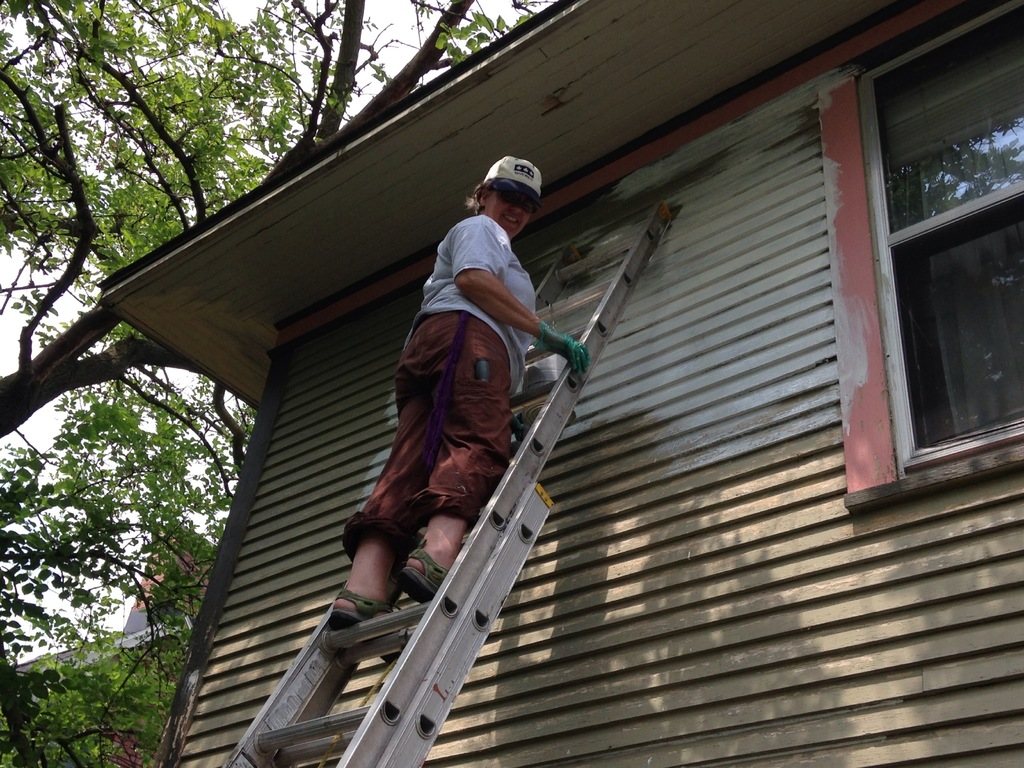 Renovation worker on a ladder fitting new siding to the side of a house