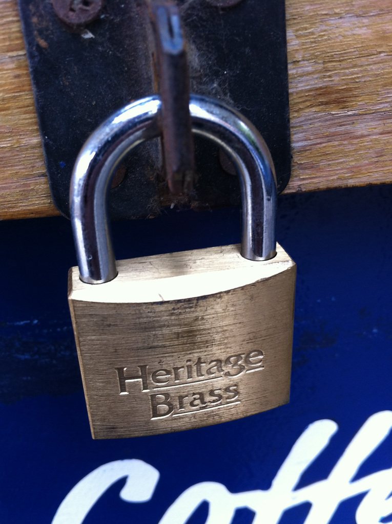 Solid brass padlock fastened through a hasp on a wooden door